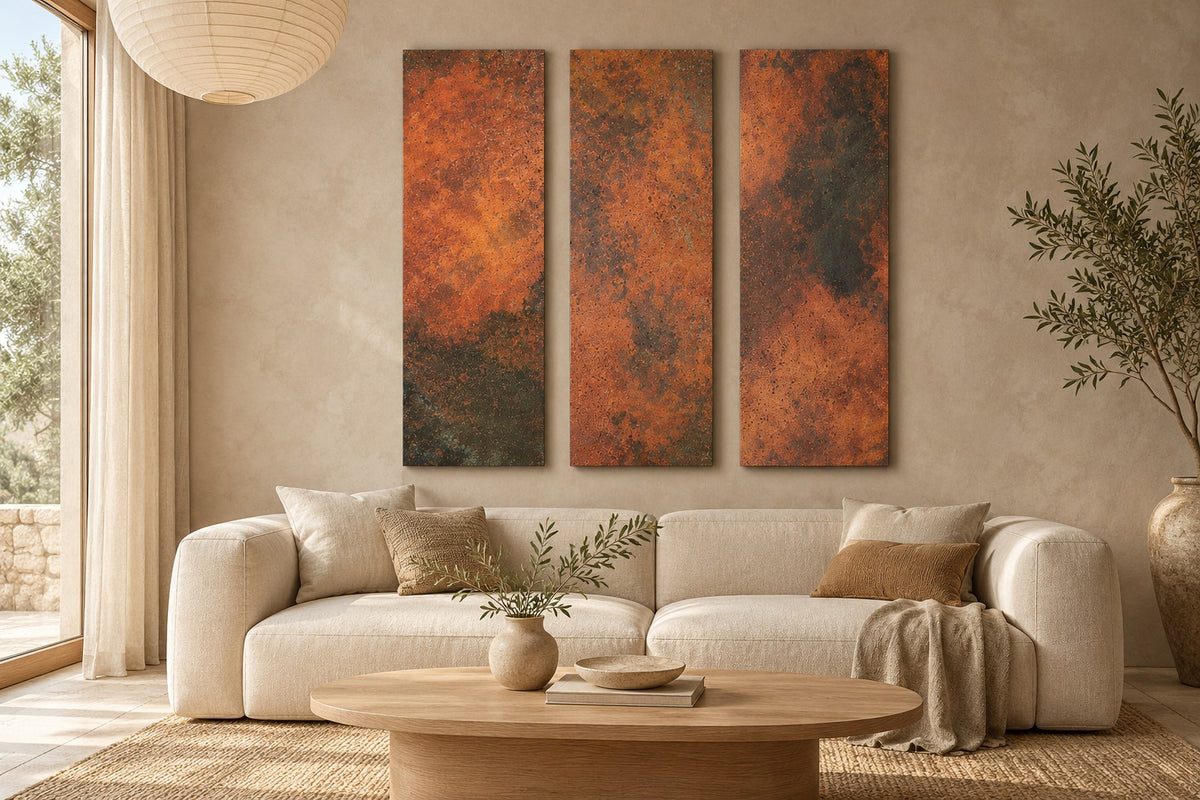 Eternal Copper Inferno – 3 pionowe panele z prawdziwej miedzi z ognistą, pomarańczowo-rdzawą patyną i grafitowymi przebarwieniami nad kremową sofą w jasnym salonie z owalnym drewnianym stolikiem i drzewkiem oliwnym